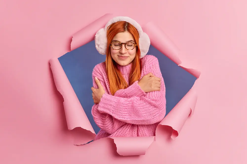 mujer abrazandoce con fondo rosado y audifonos rosados